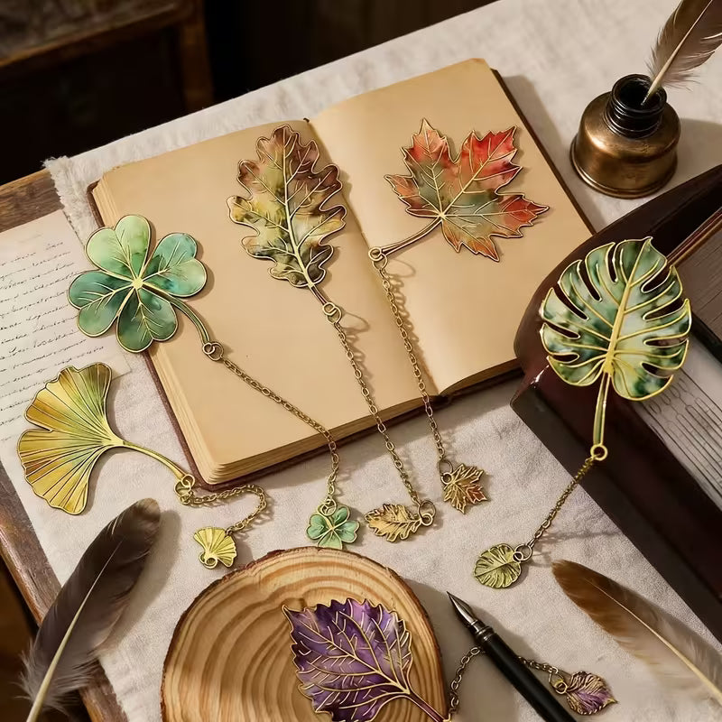 Mind a 6 vintage levél könyvjelző nyitott antik könyvön — ginkgo, lóhere, tölgy, juhar, monstera, lila levél, tolltartóval