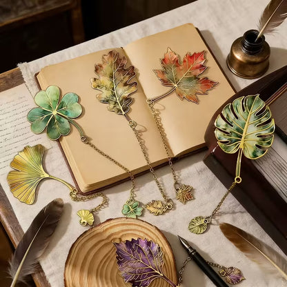 Mind a 6 vintage levél könyvjelző nyitott antik könyvön — ginkgo, lóhere, tölgy, juhar, monstera, lila levél, tolltartóval