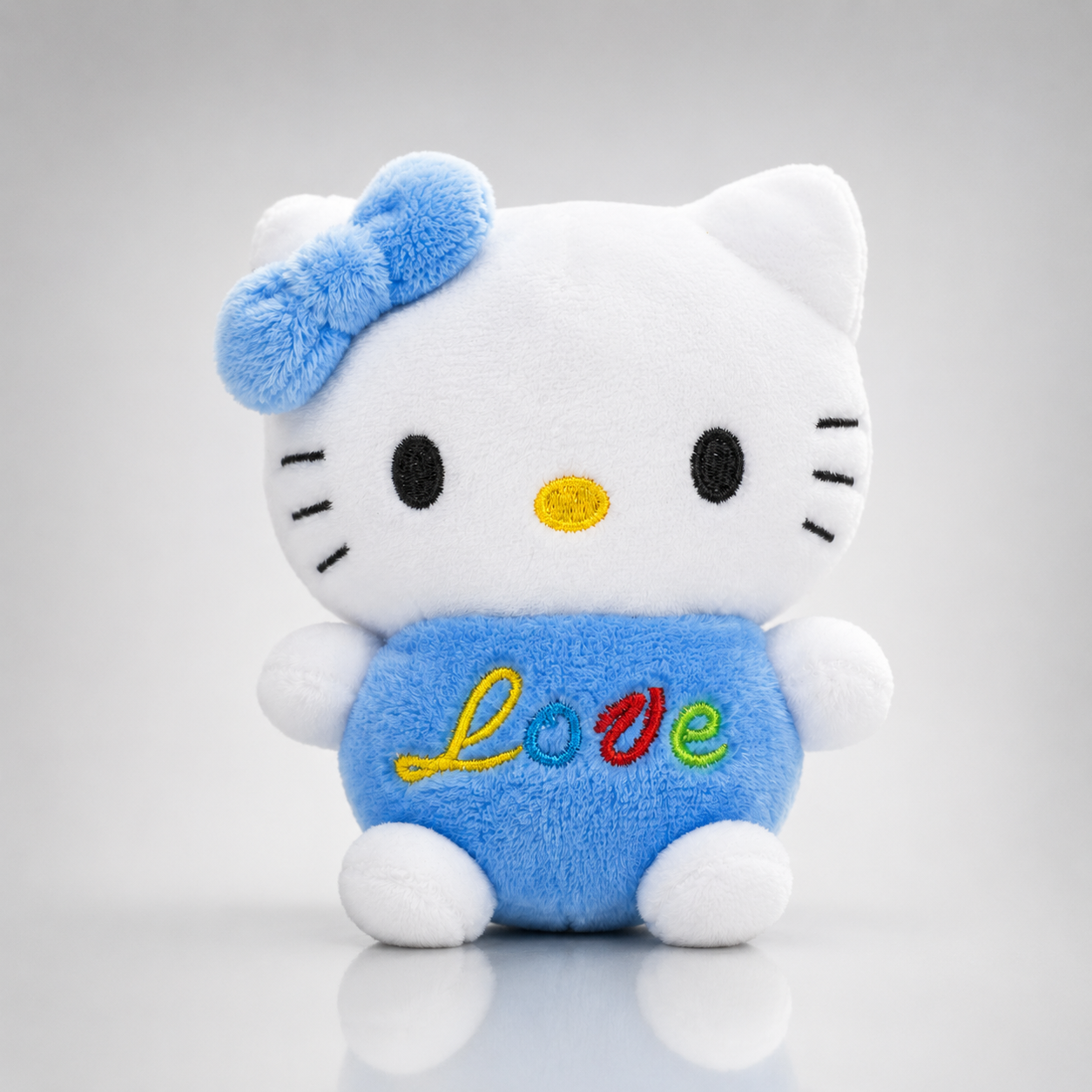 Világoskék Hello Kitty plüss figura kék masnival és színes Love feliratos szívvel.
